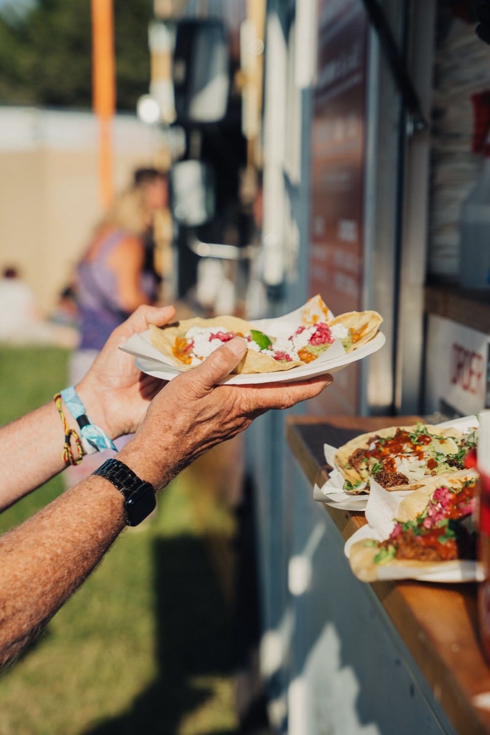 A plate of tacos handed across the counter at the hatch, more plated up on the ledge in the evening sun.