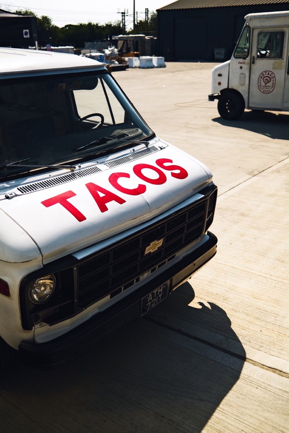 The Chevy day van with TACOS painted across the bonnet, parked up beside the step van.