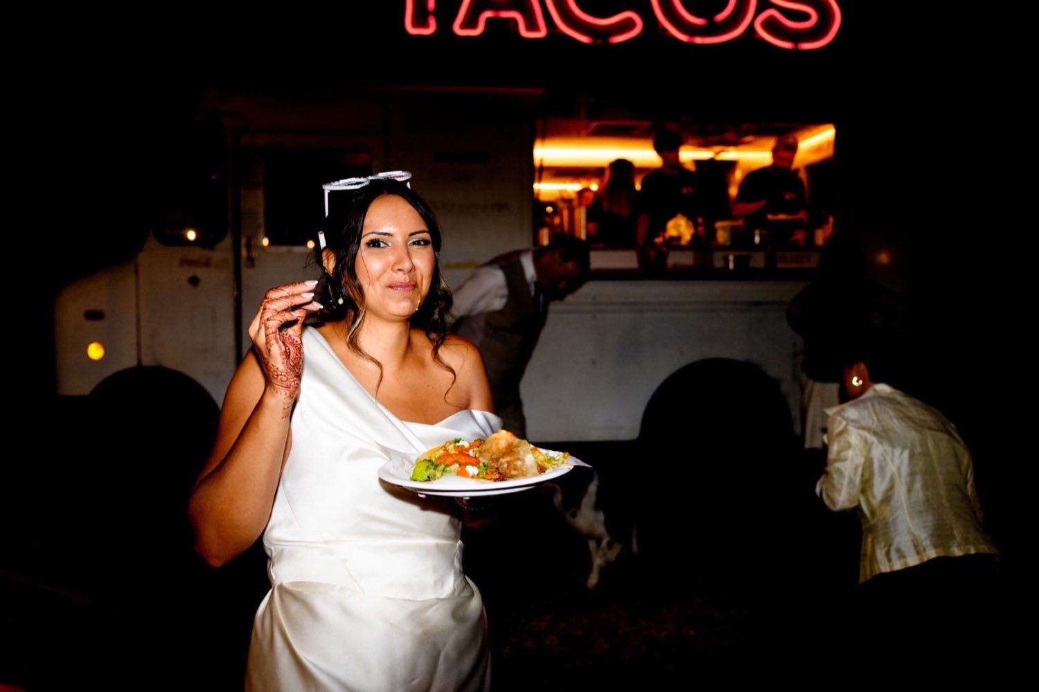 The bride holding a plate of tacos in front of the truck at night.