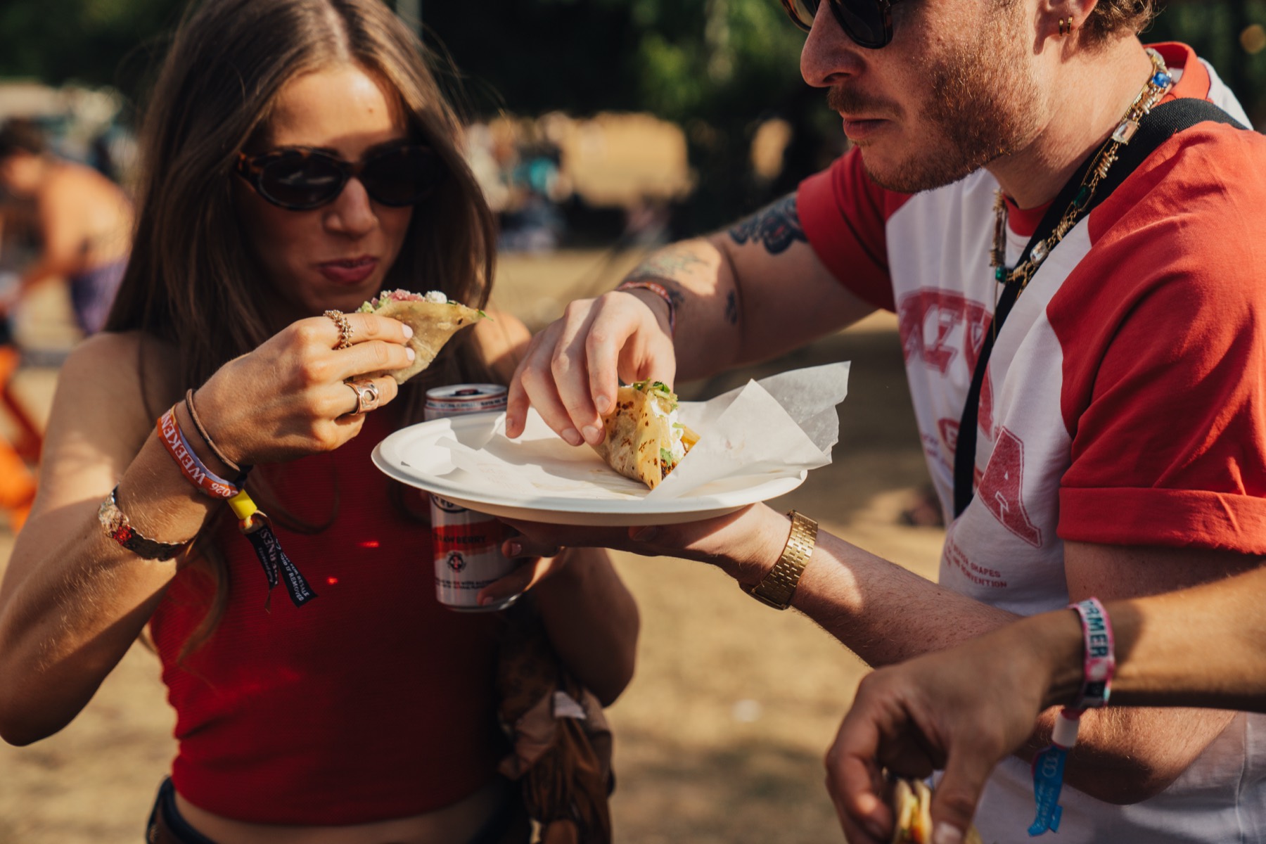 Two guests eating tacos together in the sun, plates in hand.