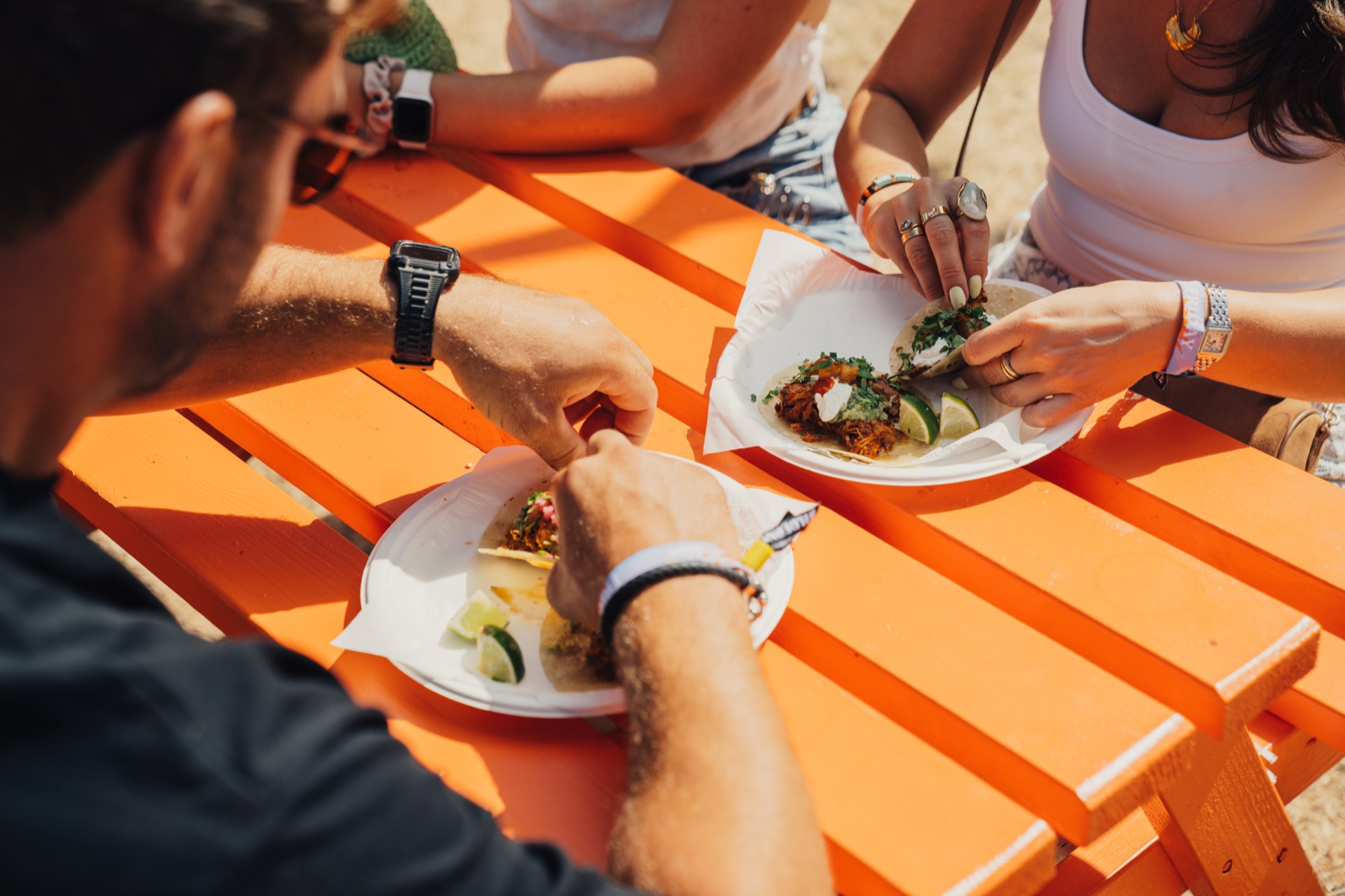 Guests round a table eating tacos, plates and hands everywhere, shot from above.
