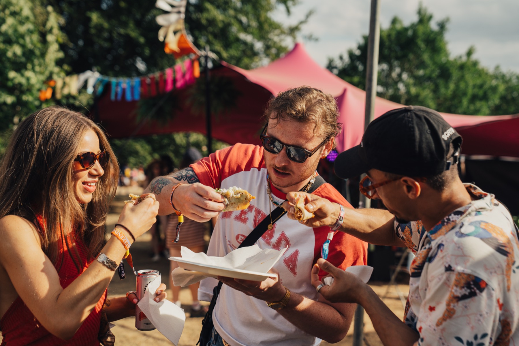 Three guests stood together eating tacos at a festival in the sun.